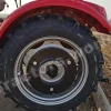 Close-up of a red tractor rear wheel with a chunky tread tire and silver rim on a farm surface.