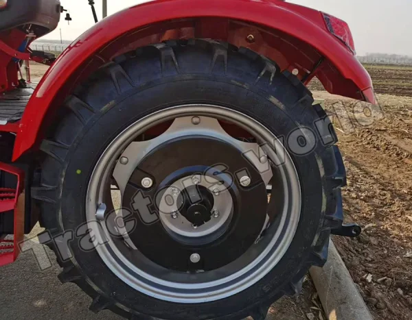 Close-up of a red tractor rear wheel with a chunky tread tire and silver rim on a farm surface.